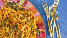 a plate with pasta and spinach on it next to gold forks, knives and spoons