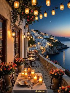 an outdoor dining area with candles and flowers on the table next to the water at dusk