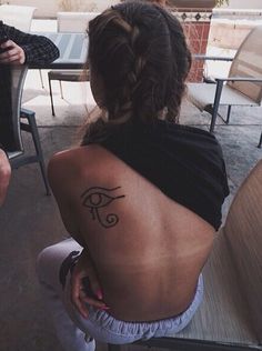 a woman with a tattoo on her back sitting in front of a table and chairs