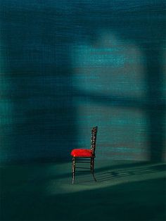 a red chair sitting in the middle of a room next to a wall with a shadow cast on it