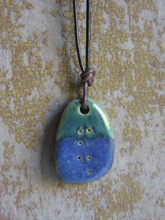 a blue and green ceramic pendant hanging on a leather cord with a bead around it