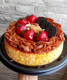 a cake decorated with cookies and strawberries on top of a black platter in front of a brick wall