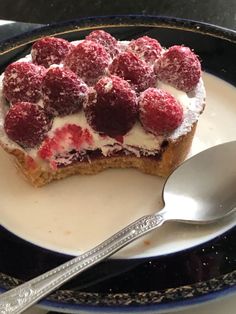 a dessert with raspberries and cream is on a plate next to a spoon