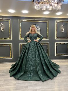 a woman standing in front of a wall wearing a green gown with long sleeves and a train