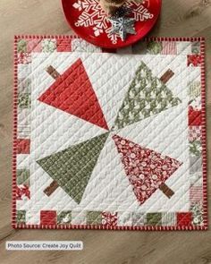 a quilted placemat with christmas trees and snowflakes on it, sitting next to a red plate