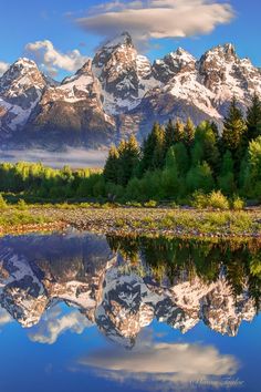 the mountains are reflected in the still water on the lake's surface, with trees and grass around them