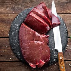 some meat is on a black plate next to a knife