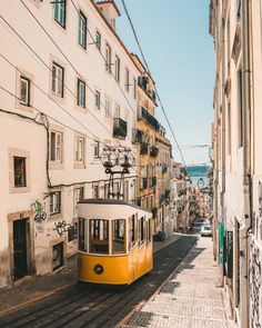 a yellow trolley car traveling down a street next to tall buildings with graffiti on the walls