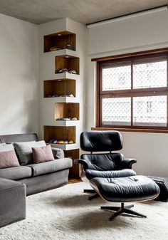 an eames chair and ottoman in front of a window with shelves on the wall