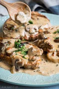 a blue plate topped with meat covered in mushroom gravy and a wooden spoon