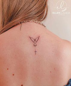 the back of a woman's neck with a small cross and dove tattoo on it