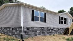 a gray house with black shutters on the front and stairs leading up to it