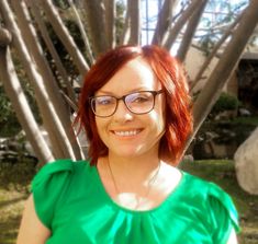 a woman with red hair and glasses standing in front of some tree branches smiling at the camera