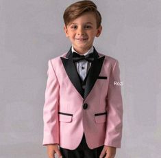 a young boy wearing a pink suit and black bow tie