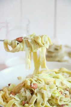 a spoon full of pasta and vegetables being lifted from a white bowl with another dish in the background