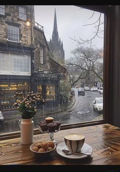 coffee and doughnuts sit on a wooden table in front of a window overlooking the street