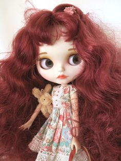 a close up of a doll with long red hair and a teddy bear in her hand