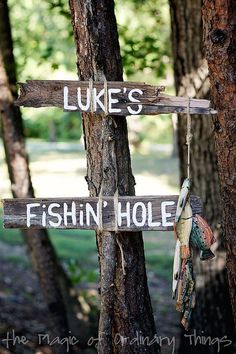 a wooden sign that says luke's fishin hole hanging from a tree in the woods