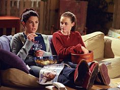 two women sitting on a couch eating food and talking to each other in the living room