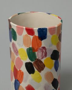 a multicolored ceramic vase with spots on the outside and inside, sitting on a gray surface