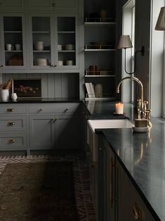 a kitchen with gray cabinets and marble counter tops, along with a gold faucet