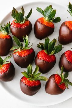 chocolate covered strawberries are arranged on a white plate with green leaves and sprinkles