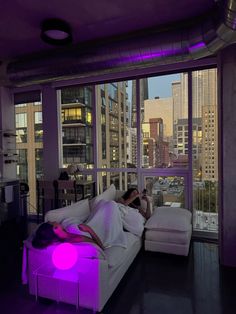 a person laying on a couch in front of a window with city lights behind them