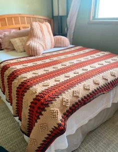 a bed with a blanket and pillows on top of it in a bedroom next to a window