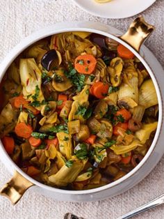 a white bowl filled with vegetable stew next to two silver spoons on a table