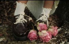 a pair of shoes with laces on them and flowers in front of them, sitting on the ground