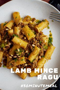 a white plate topped with pasta covered in meat and pine nuts next to a fork