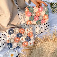 a woman is holding a crocheted purse on a table with flowers and straw