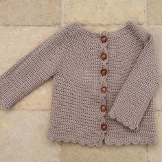 a crocheted sweater with buttons on the front and back, sitting on a tile floor