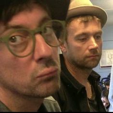 two men wearing glasses and hats are looking at something in front of the camera while another man looks on