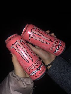 two cans of monster energy drink being held by someone