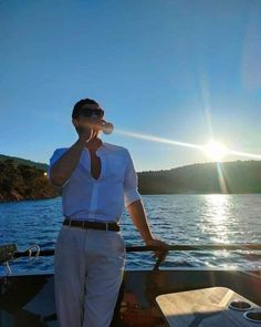 a man standing on the deck of a boat talking on a cell phone while wearing sunglasses