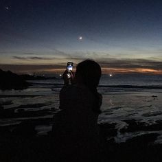 a person taking a photo with their cell phone at night on the beach by the ocean