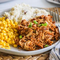 a white plate topped with corn and pulled pork next to mashed potatoes on a wooden table