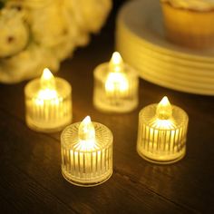 four lit candles sitting on top of a wooden table next to cupcakes and flowers