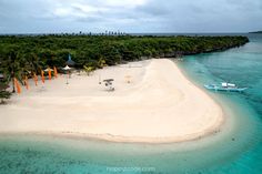 an aerial view of a beach with boats and palm trees in the distance, surrounded by blue water