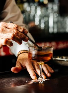 a man is holding a spoon in his hand while sitting at a bar with a drink