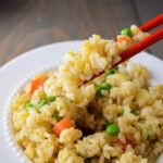 rice with peas and carrots in a white bowl on a plate, with chopsticks