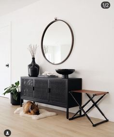 a dog laying on the floor in front of a mirror and table with vases