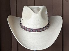 Chet starts with a Mexican soft palm leaf hat body that has a 3 3/4" brim and 5 1/4" crown. The band is simple with distressed brown leather and antique nickel color spots. The back of the band has a deer antler bead for accent. A neutral feather combo completes the hat. Note: Please allow 3-4 weeks. Adjustable Distressed Brown Country Hat, Adjustable High Crown Straw Hat In Natural Color, Distressed Brown Adjustable Hat With Flat Brim, Adjustable Straw Hat With Flat Crown For Country Events, Distressed Brown Adjustable Short Brim Hat, Distressed Brown Adjustable Flat Brim Hat, Distressed Brown Adjustable Hat For Western-themed Events, Adjustable Distressed Brown Hats For Rodeo, Rustic Adjustable Hat Bands In Distressed Brown