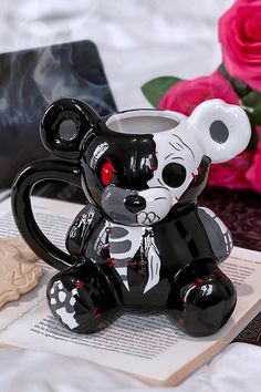 a black and white bear mug sitting on top of an open book next to pink roses