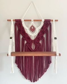 a macrame wall hanging on a wooden shelf with white and red tassels