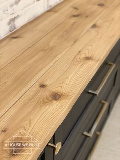 a wooden counter top in a kitchen with black drawers and white brick wall behind it