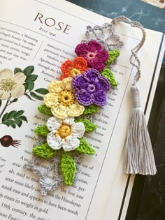 a bookmark with crocheted flowers and tassels on top of an open book