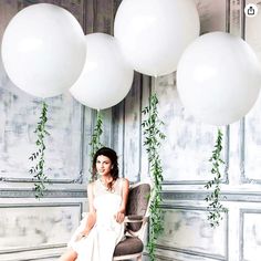 a woman is sitting in a chair with white balloons hanging from the ceiling above her