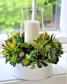 a white vase filled with green plants and a lit candle on top of a window sill